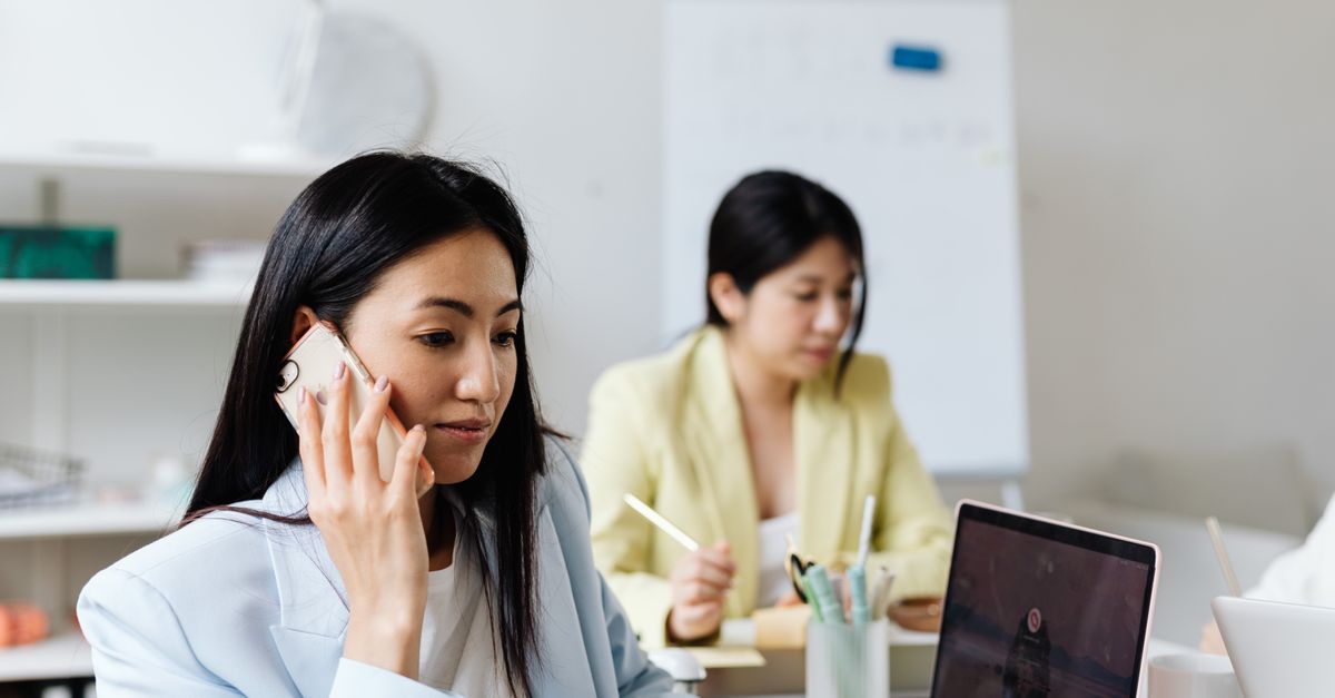 Businesswoman using phone and laptop in a modern office setting.