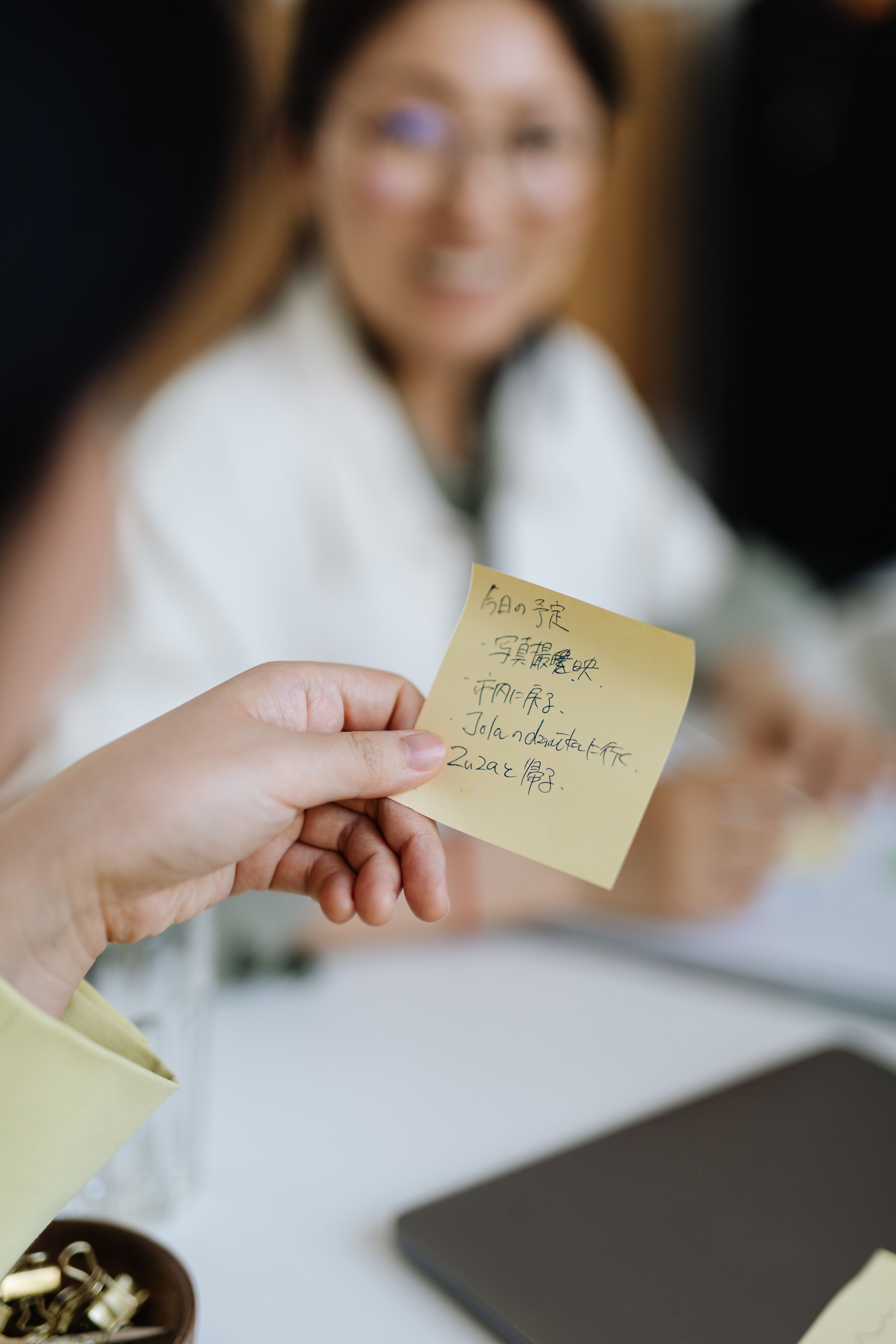 A close-up shot of a hand writing on a sticky note with a pen, with a blurred background of other sticky notes.