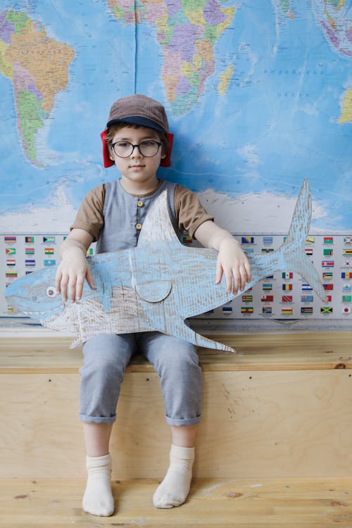 Boy Sitting with a Cardboard Shark by a World Map