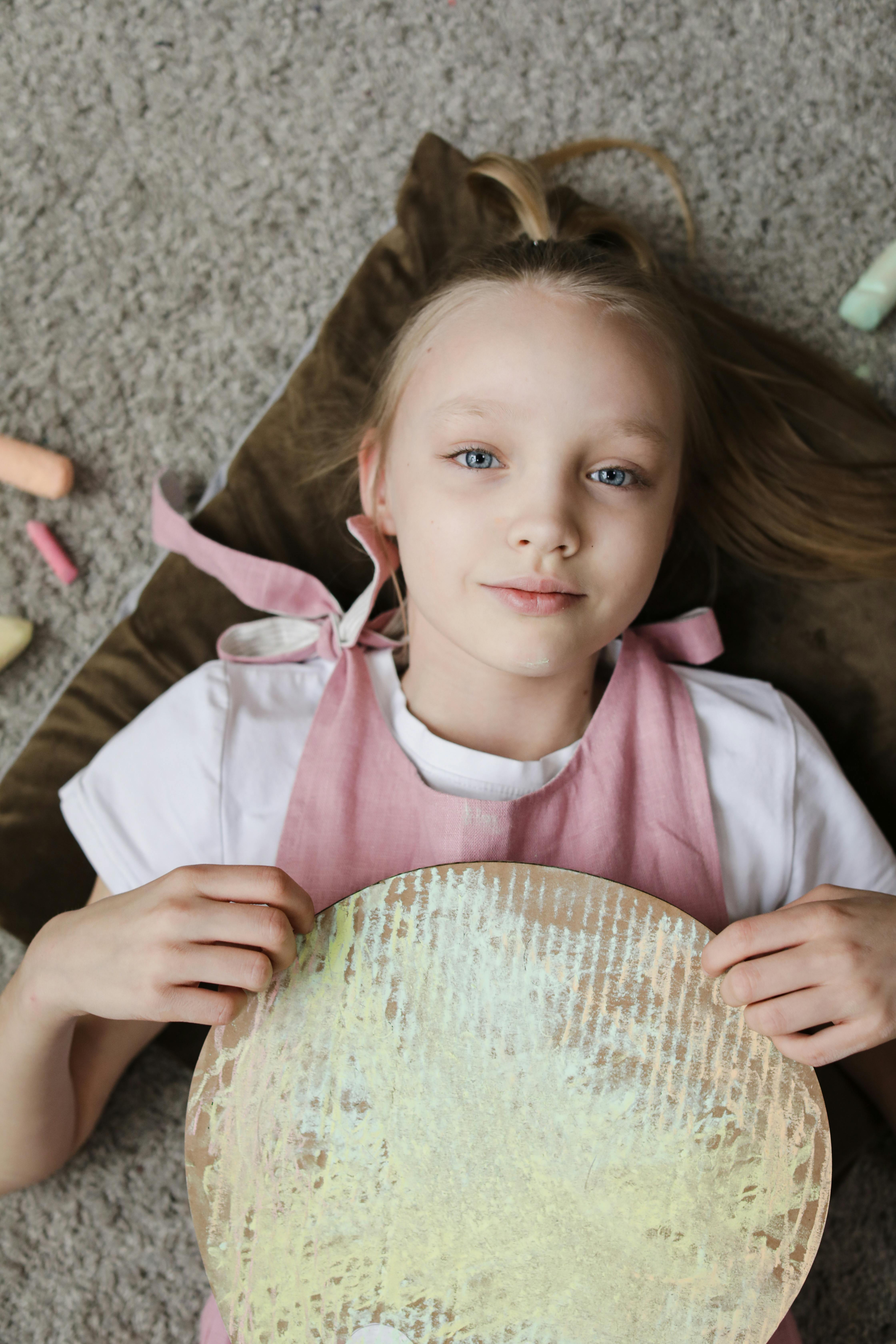 Young girl lying on floor holding artistic craft. Capturing creativity and innocence.