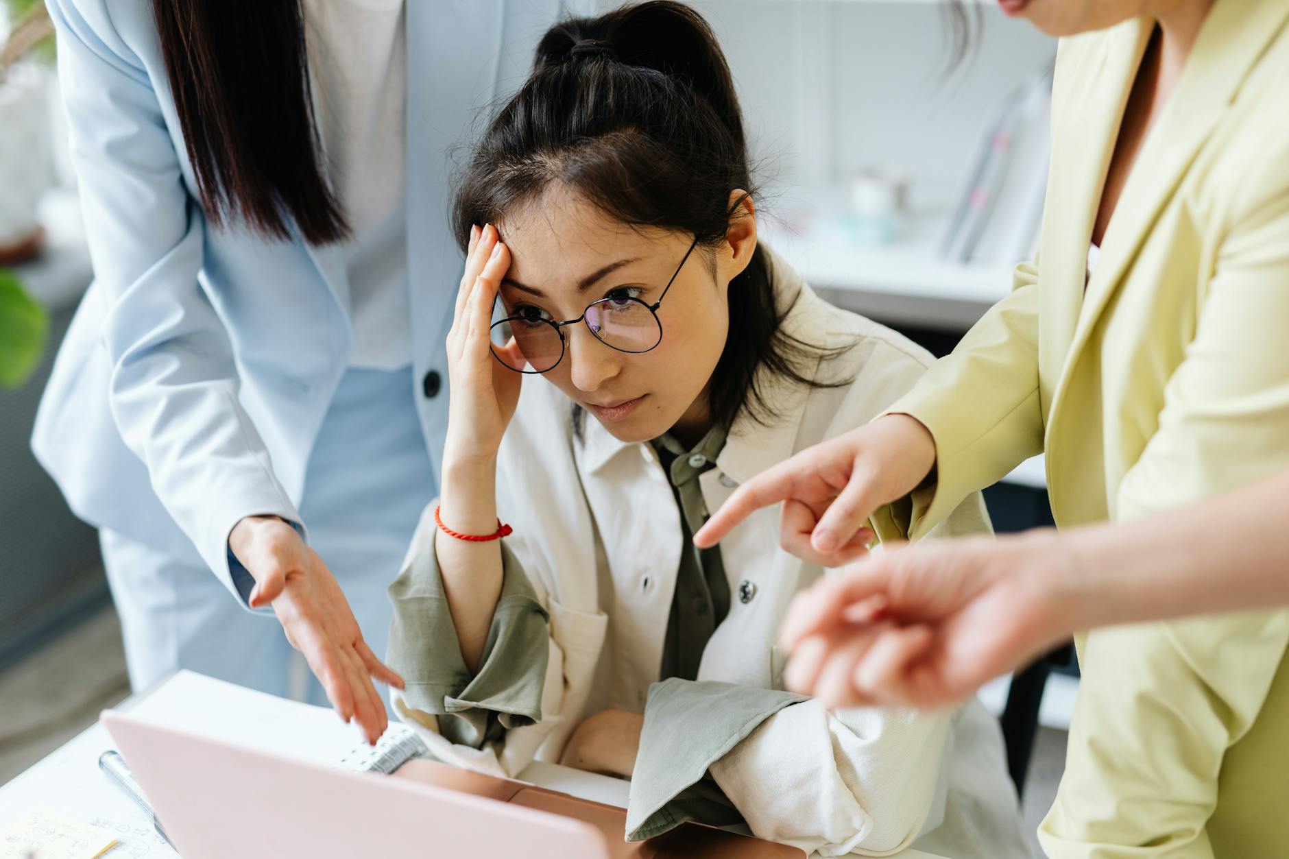 Tired woman with coworkers discussing a project in the office at a laptop, expressing frustration.