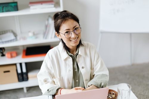 Free Smiling woman in glasses working on a laptop at a contemporary office desk. Stock Photo