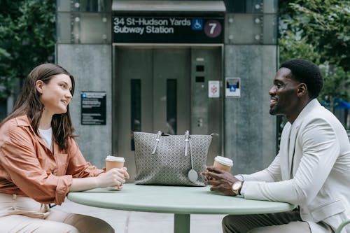 Young Man and Woman Sitting at a Table, Drinking Coffee and Talking 