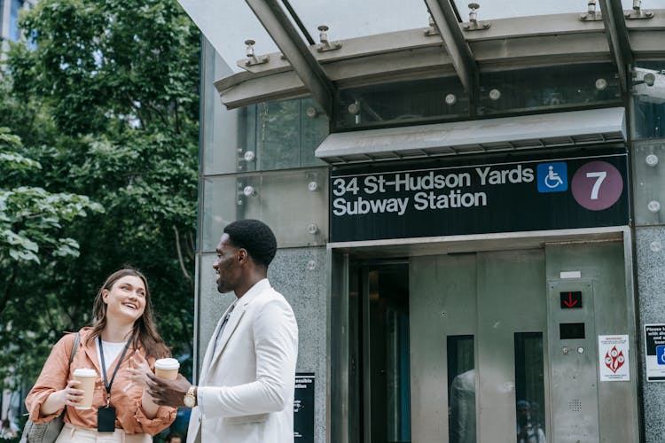 Young Man And Woman With ID Badges Standing And Talking In Front Of An Elevator Entrance To A Subway Station 