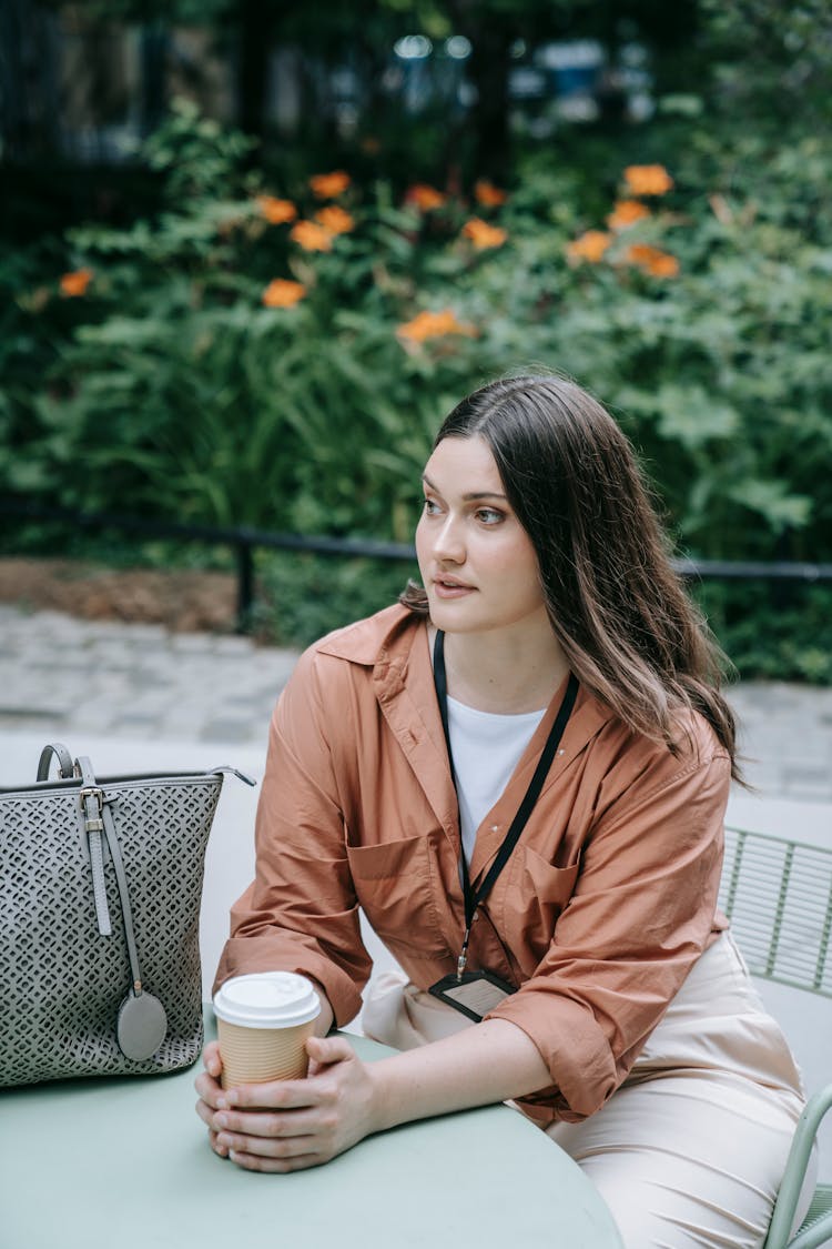 Woman With An ID Badge Sitting At A Table Outdoors And Drinking Coffee 