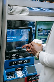 Close-up of a person using a subway ticket machine with a credit card and coffee cup.