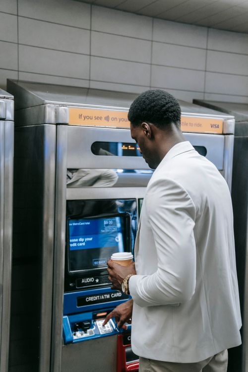 Free Businessman with coffee uses ATM indoors. Finance and transactions made simple. Stock Photo