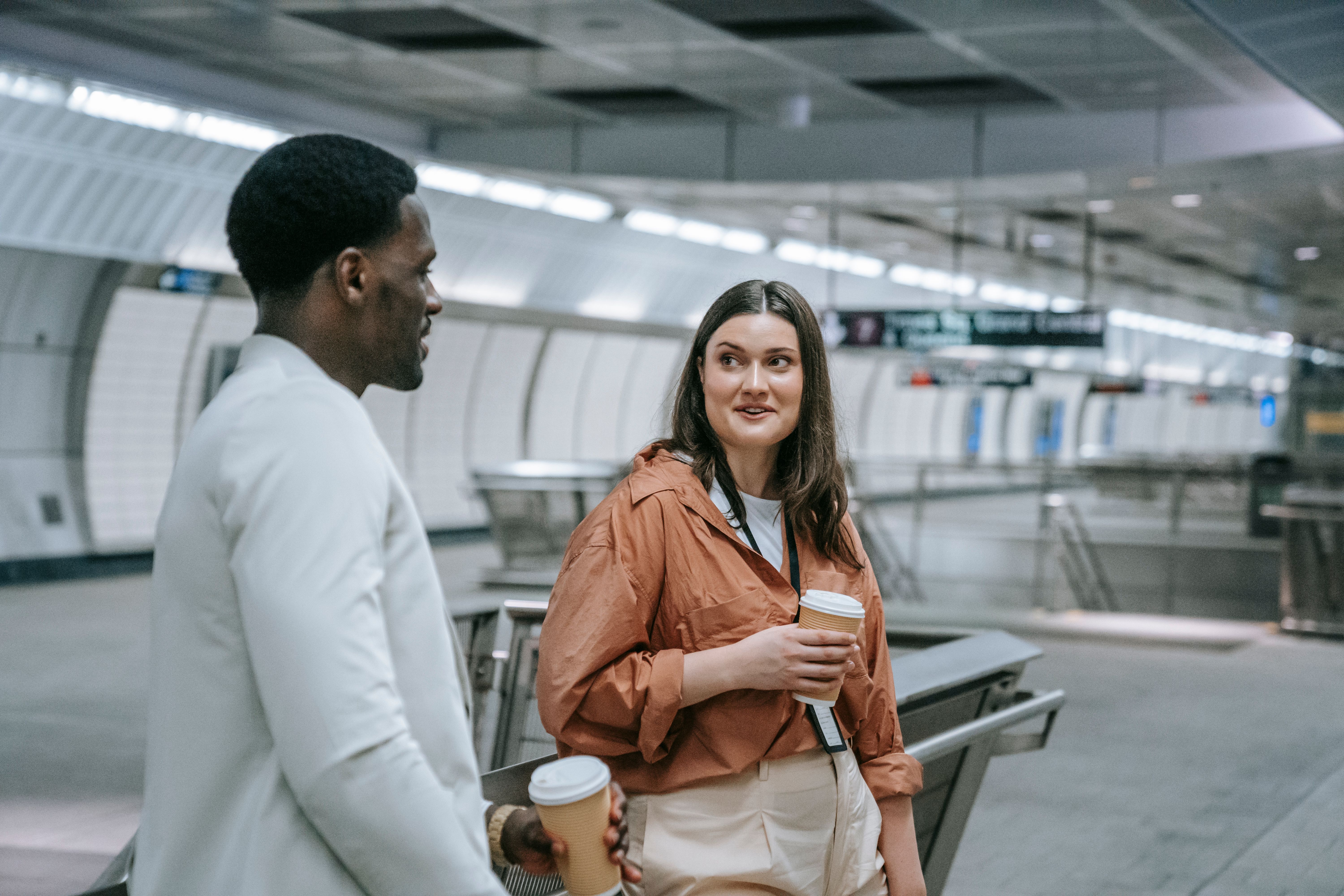 Two people having a friendly chat with coffee at a metro station, showcasing urban lifestyle.