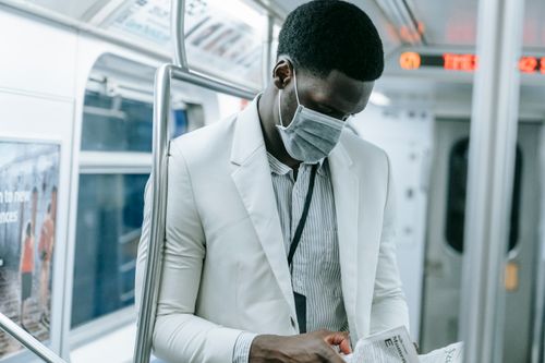Free An adult man in a face mask reads a newspaper during a train commute, highlighting urban life amid the pandemic. Stock Photo