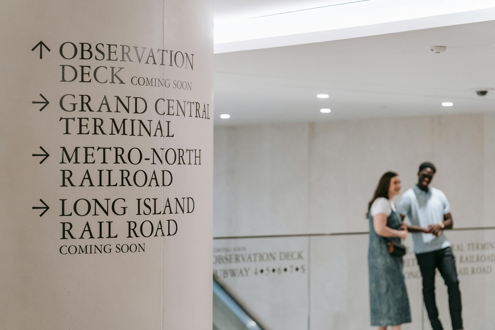 Directional signs at Grand Central Terminal with people in the background.