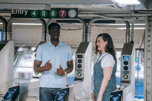 Two adults at a metro station entry turnstile having a conversation and smiling.