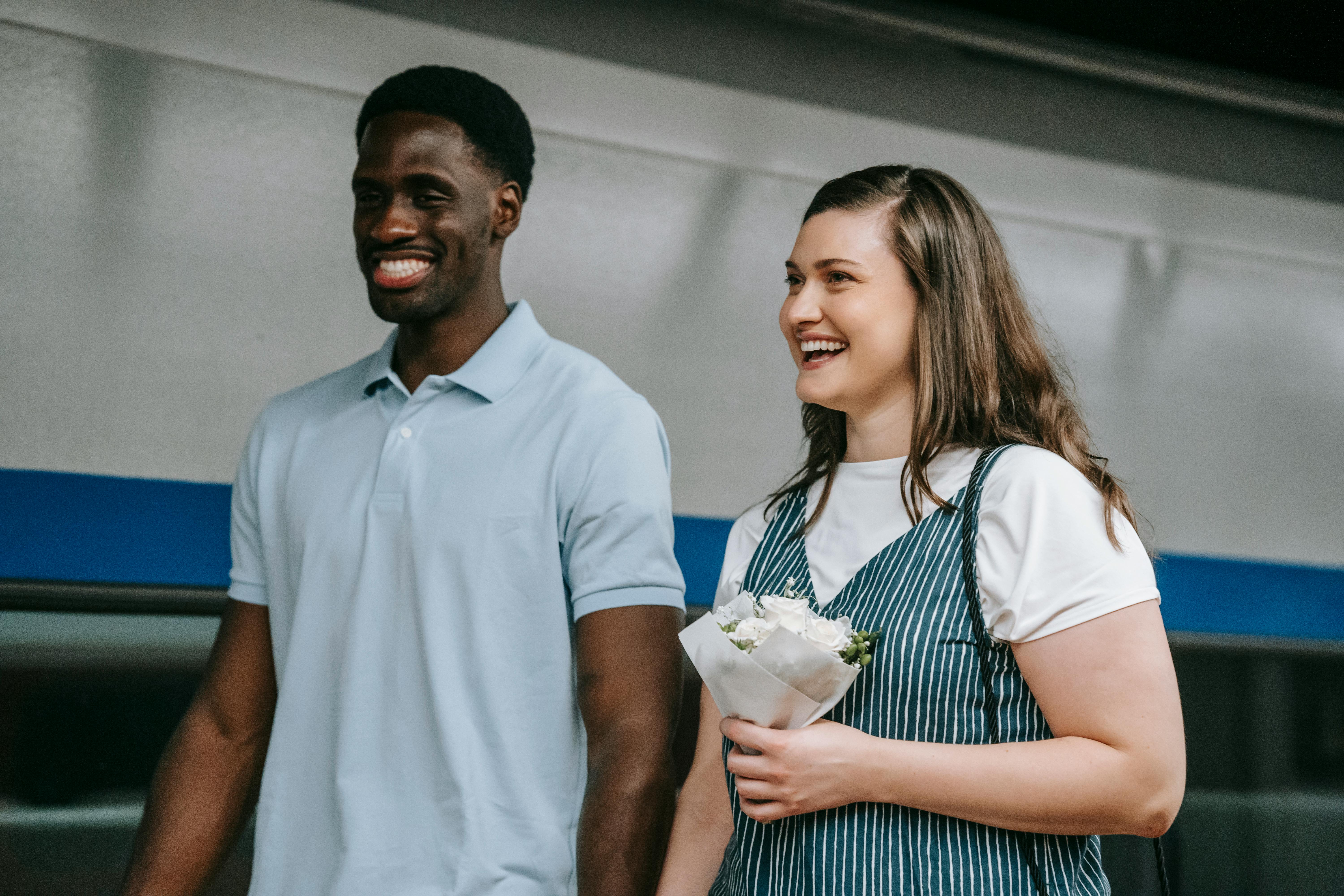 A cheerful interracial couple holding flowers, captured indoors, showcasing love and joy.