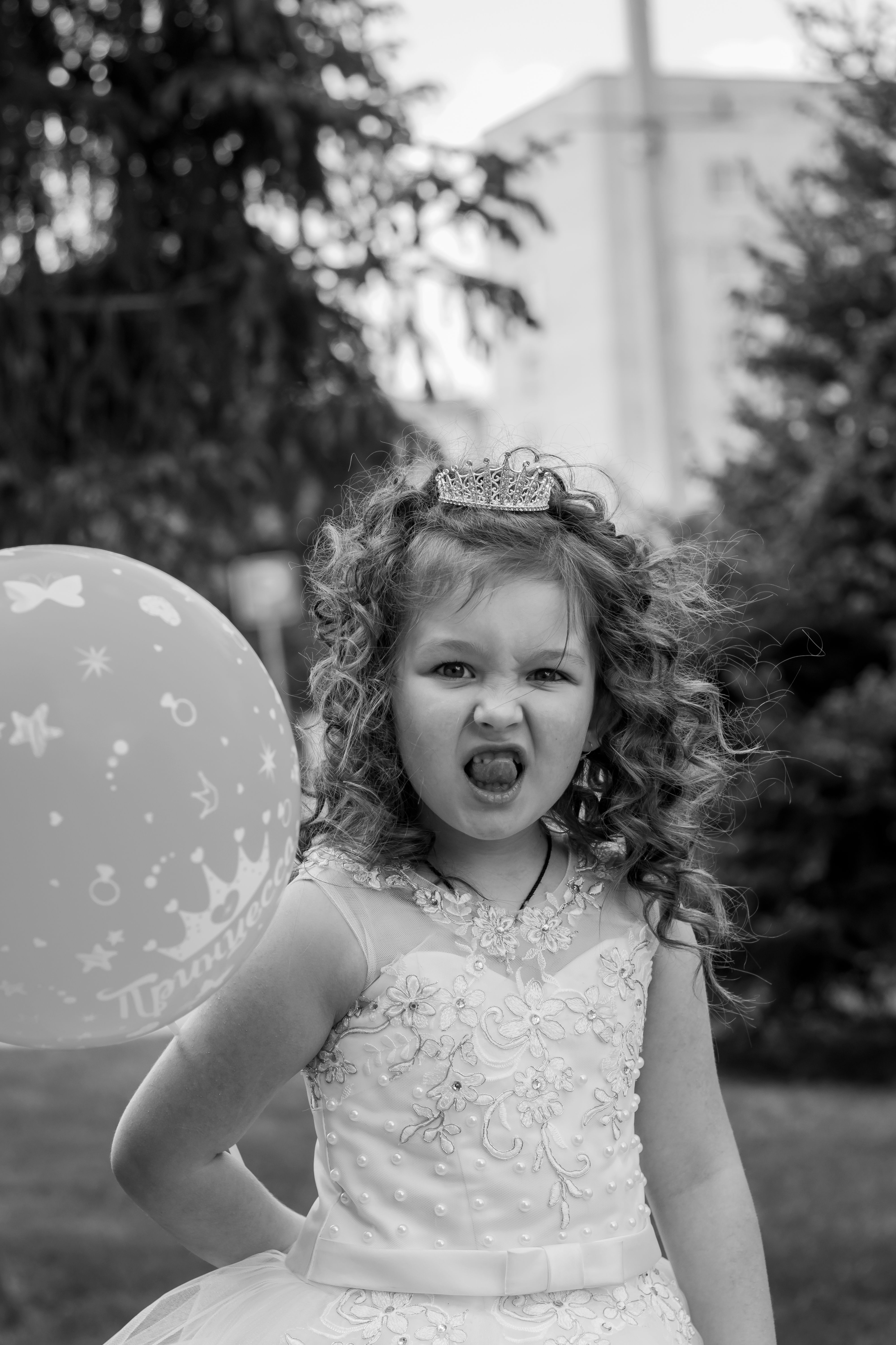 Adorable girl making a funny face while holding a balloon in a princess dress.