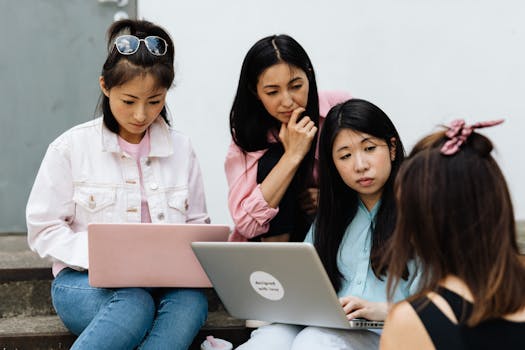Group of women using laptops for a collaborative meeting on outdoor steps, discussing ideas.