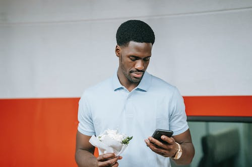 Free Man in Blue Polo Shirt Holding Cellphone and Flowers Stock Photo