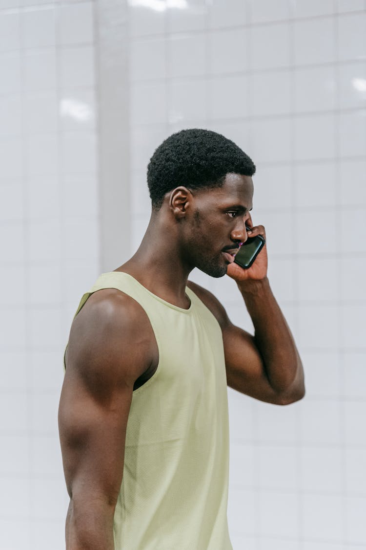 A Side View Of A Man Wearing Tank Top While Talking On The Phone