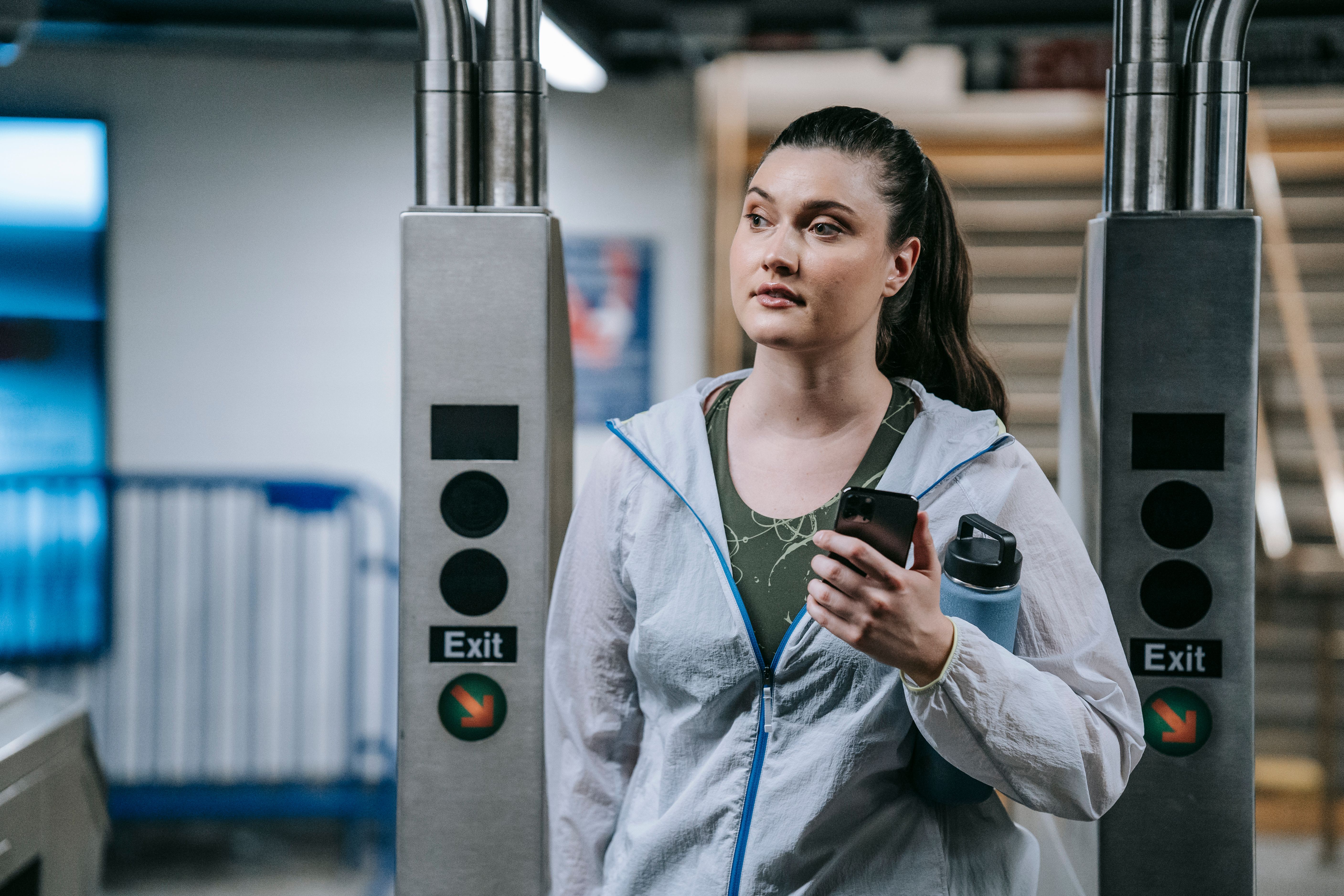 A woman in sports clothing exits a modern subway station holding a smartphone.