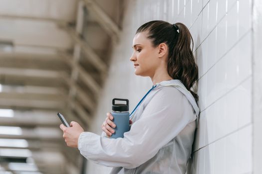 Woman in sportswear holding water bottle and smartphone in subway station.