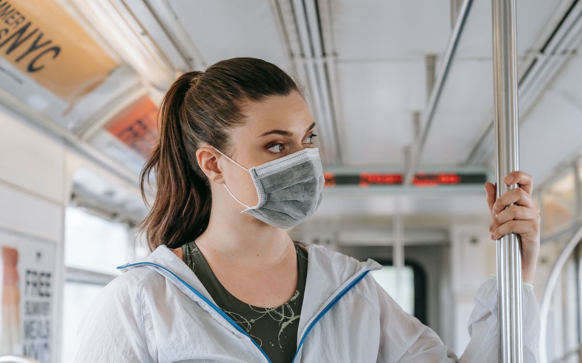 An adult woman wearing a face mask rides public transportation, focusing on safety and protection.