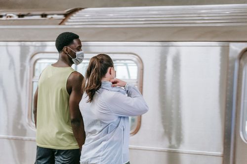 Free Two people standing on a subway platform wearing masks, waiting for the train. Stock Photo