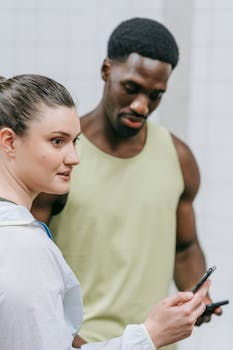 Two adults engaged in discussion while holding mobile phones, casual setting.