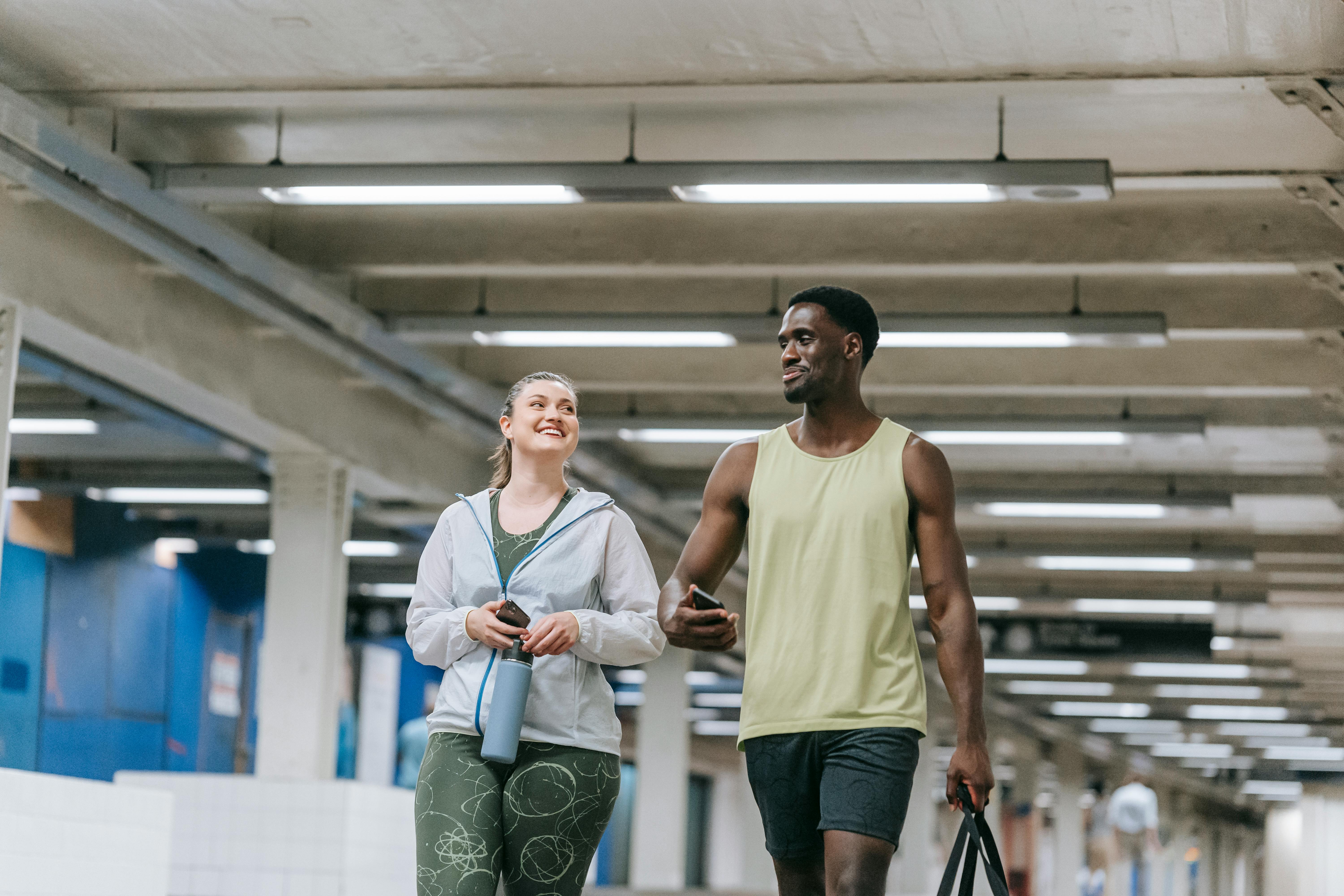 Smiling couple in sportswear walking indoors, promoting health and fitness.