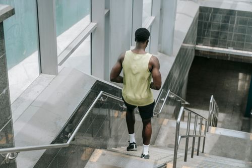 Free Back view of a muscular man in a tank top running down indoor stairs, focusing on fitness and movement. Stock Photo