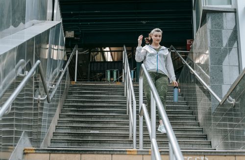 Free Woman in sportswear descending stairs, holding a water bottle, outdoors. Stock Photo