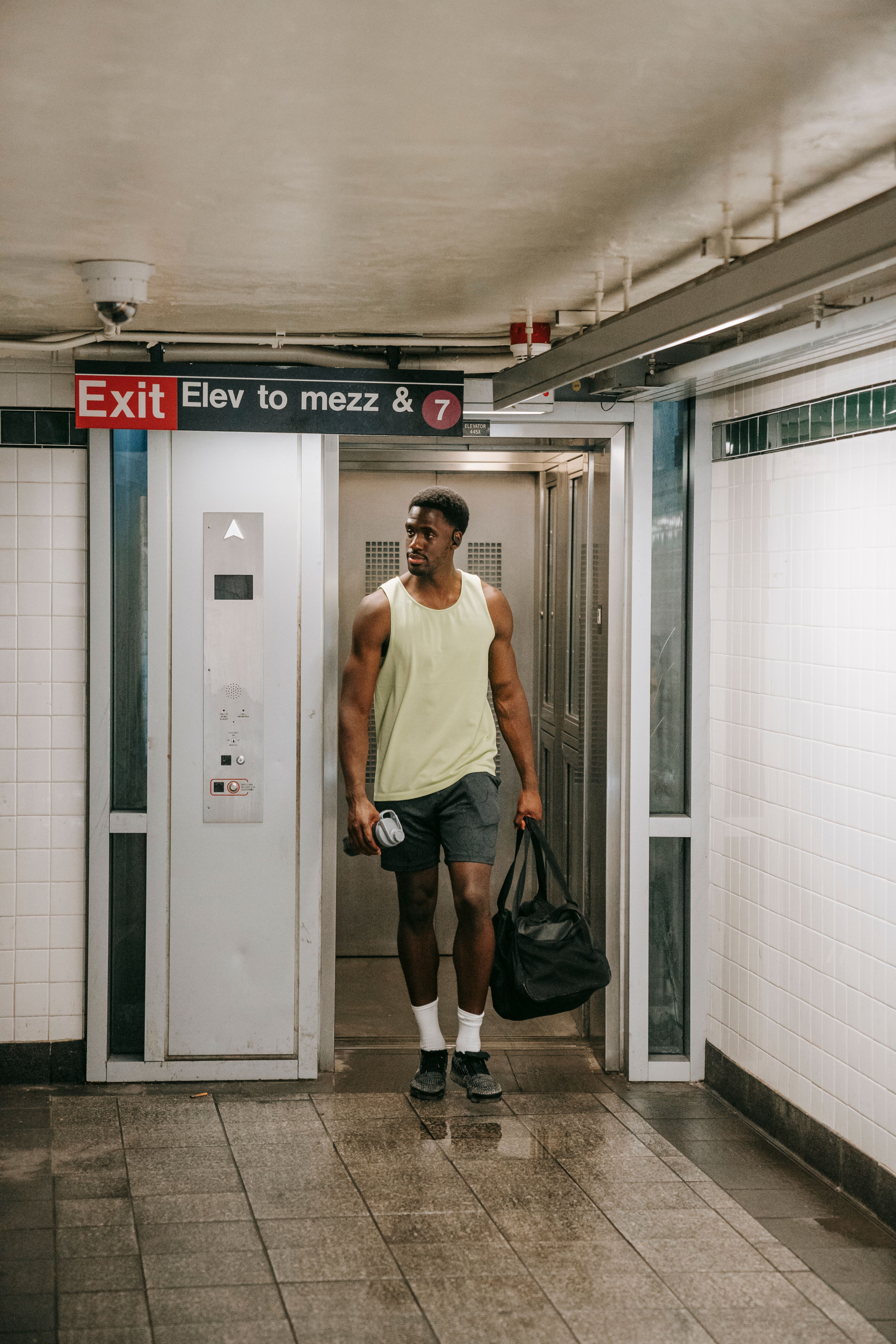 Athletic man leaving subway elevator with a gym bag, wearing sportswear in urban setting.