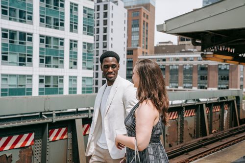 Free A stylish couple waits on a train platform in an urban setting, capturing a modern city lifestyle. Stock Photo