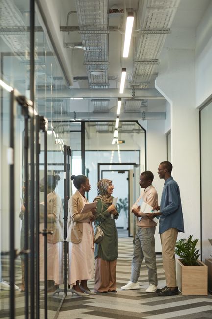 Four professionals engage in a friendly discussion in a modern office corridor.