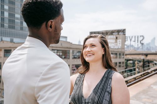 Free A happy couple smiling on a rooftop with city buildings in the background. Stock Photo