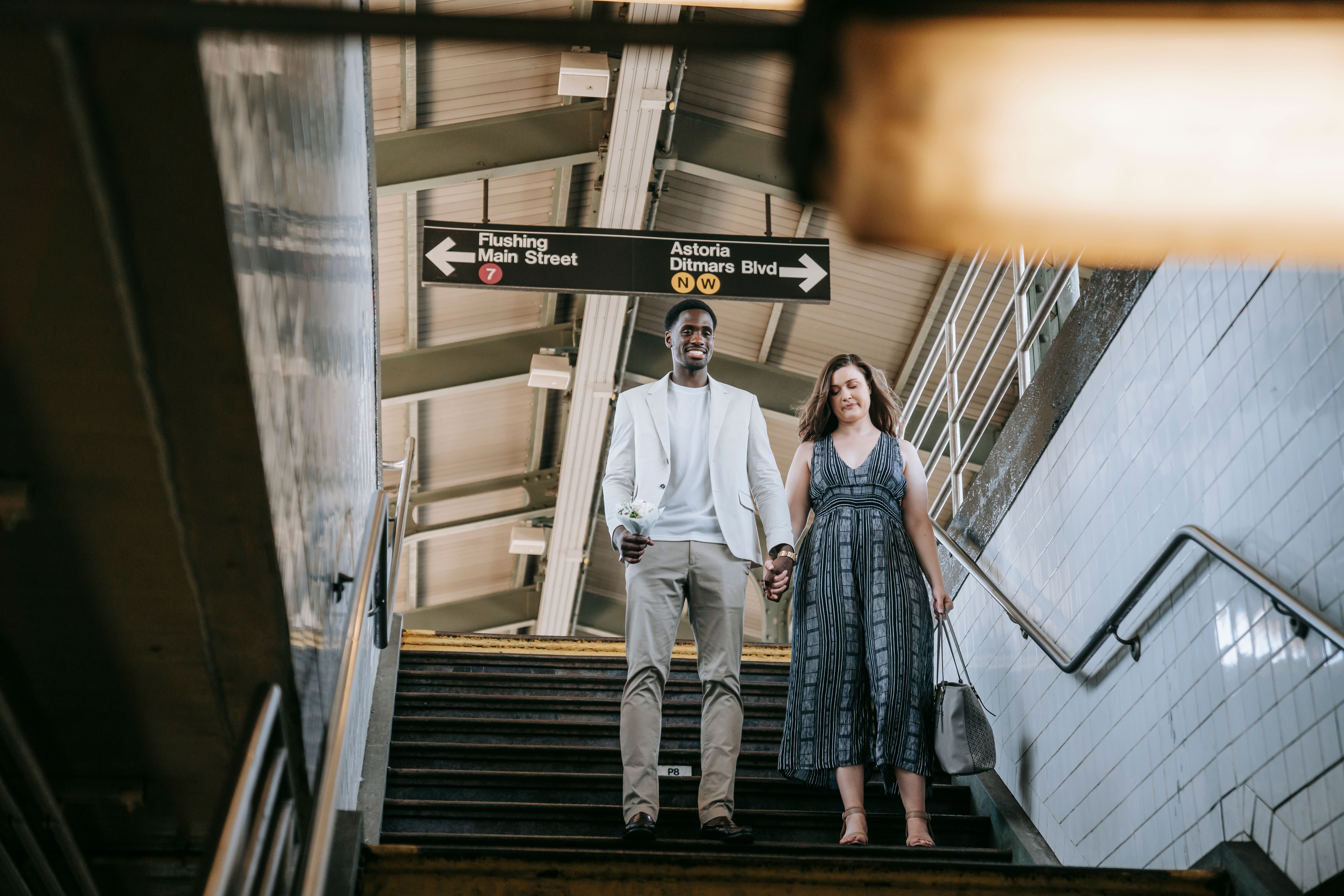 A couple walks down subway stairs holding hands, showcasing urban romance and connection.
