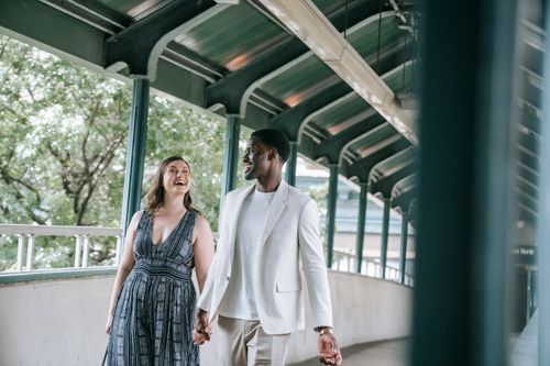 Free A joyful couple holding hands and walking together in an urban area under a covered pathway. Stock Photo