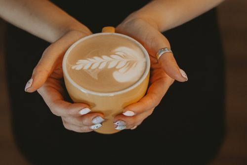 Free Woman holding a cappuccino with leaf design latte art in a cozy setting. Stock Photo