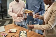 Colleagues celebrating in an office with champagne and a variety of snacks.