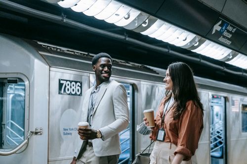 Free A couple smiling and walking at a New York City subway station, holding coffee cups. Stock Photo