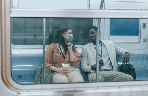Free Two people sit and converse, wearing masks, inside a subway train. Stock Photo