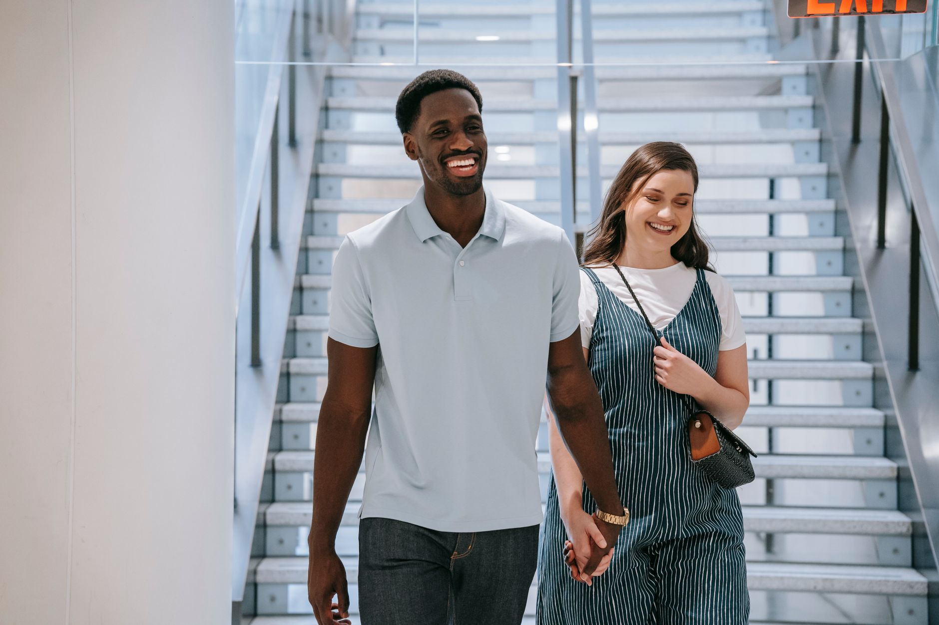 Cheerful couple holding hands and smiling while walking down a staircase indoors.