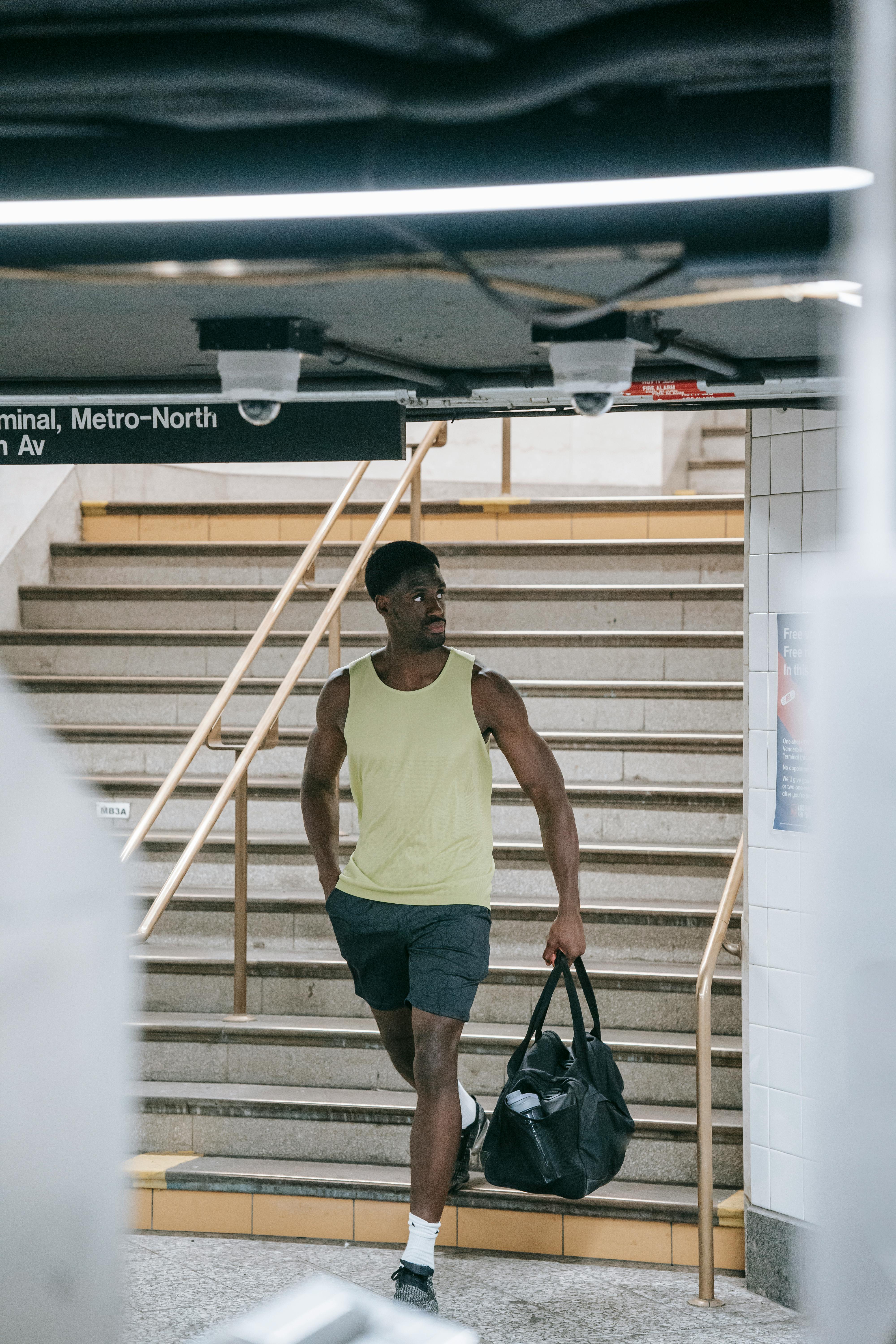 A muscular man in activewear walks through a subway station carrying a duffle bag.