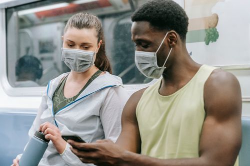 Free Couple in activewear with face masks in subway, holding phone and water bottle. Stock Photo