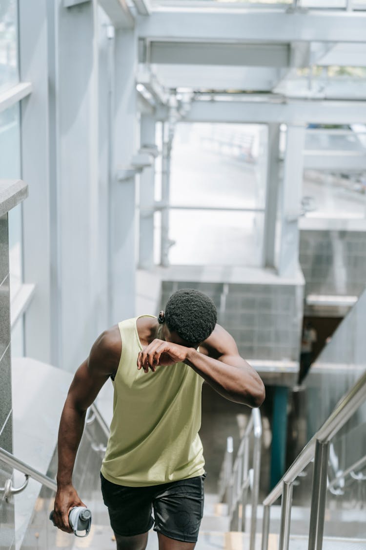 Man In Yellow Tank Top And Black Shorts Walking Up The Stairs Feeling Tired