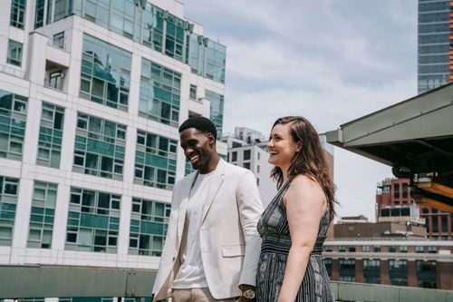 Free A happy couple walking and smiling against a modern city skyline backdrop. Stock Photo