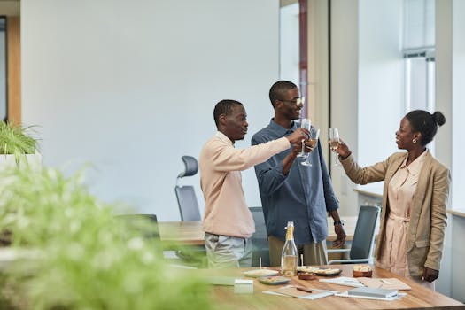 Three colleagues toasting to success with wine glasses in a modern office setting.