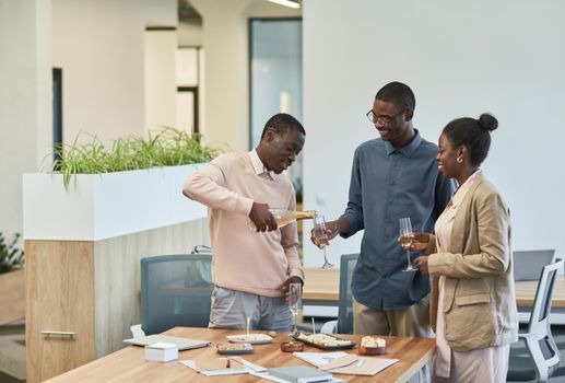 Three colleagues enjoy a celebratory toast with champagne in a modern office setting.