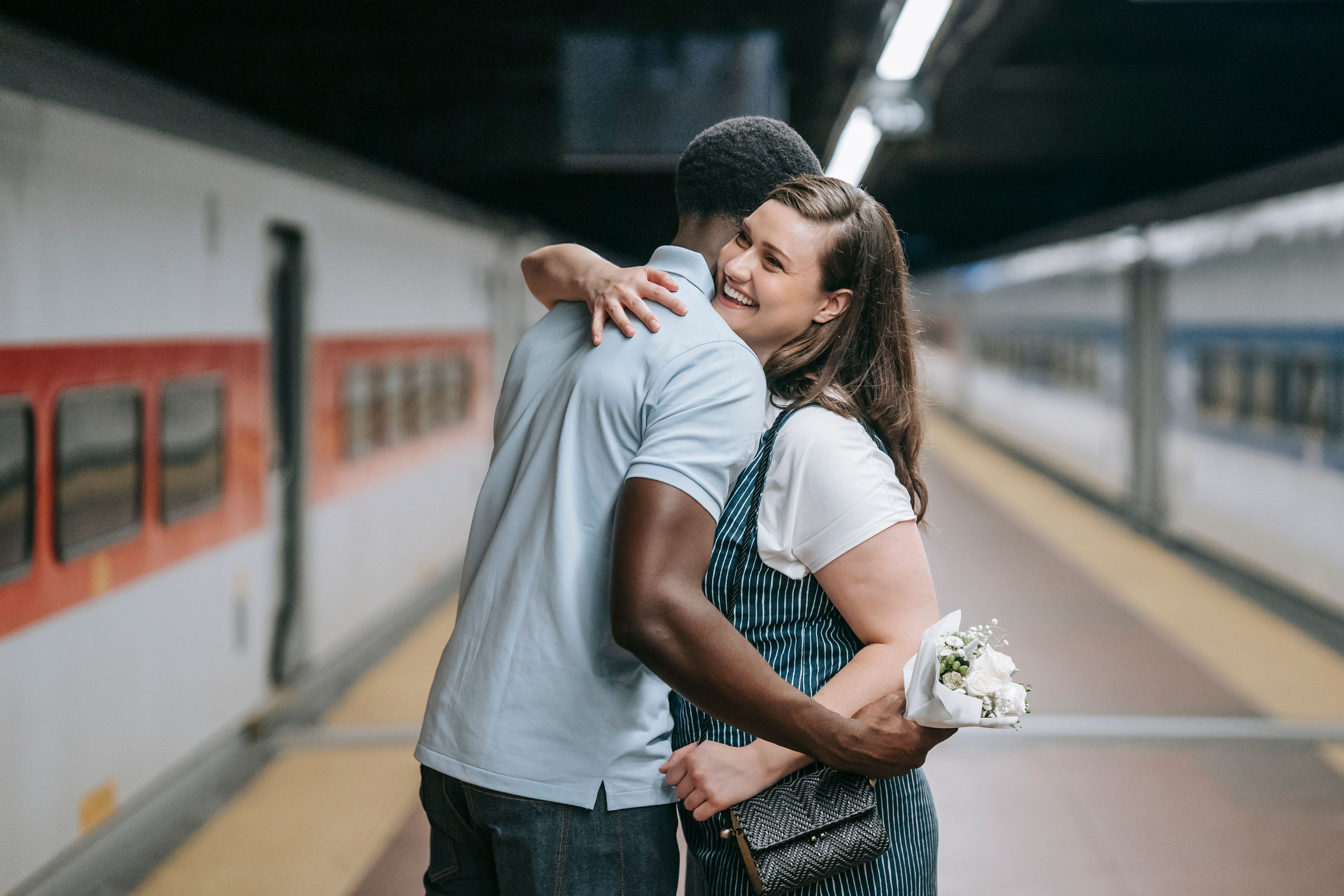 Couple embraces on a train platform while smiling beside a stopped train