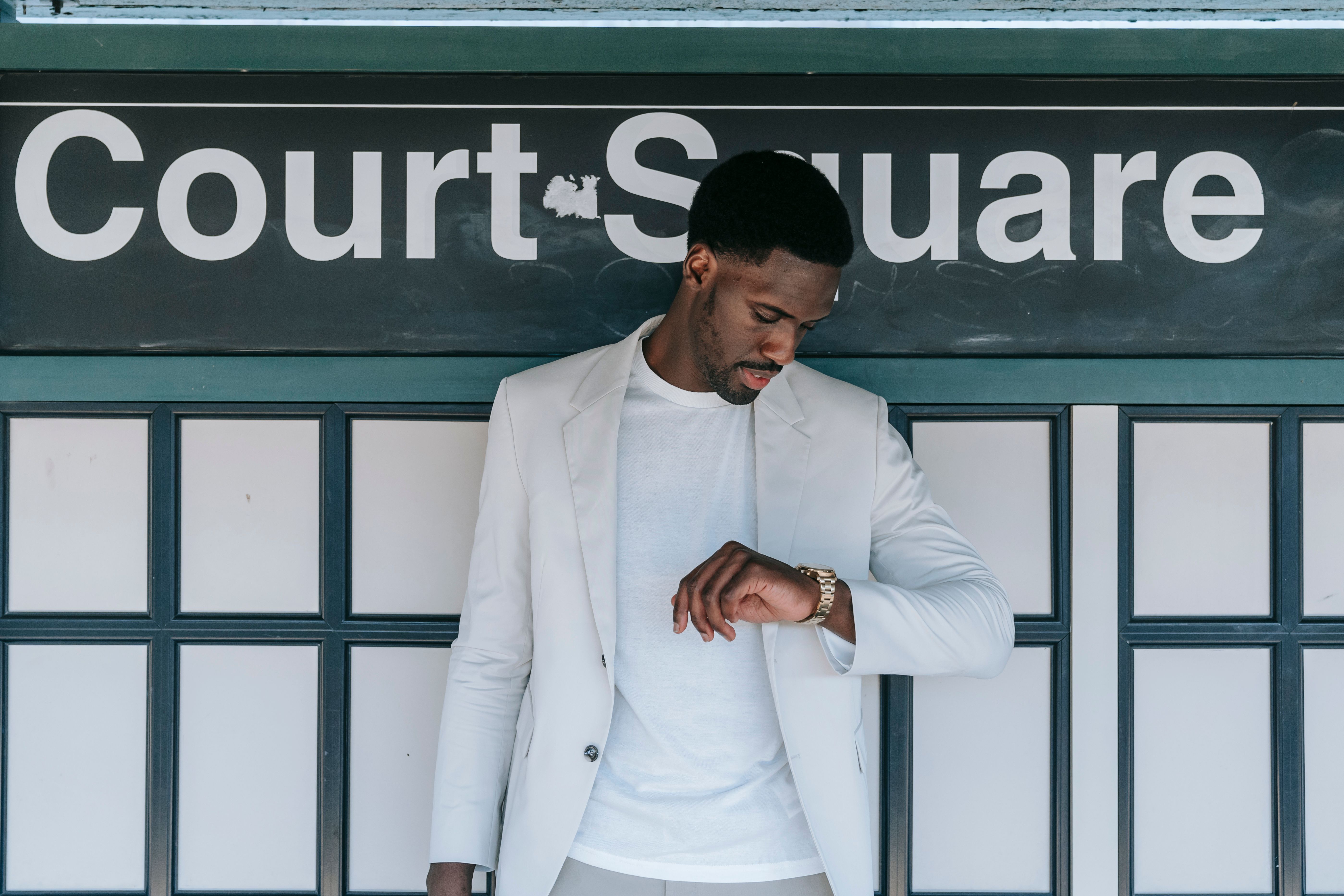 A fashionable man in a white blazer checks his wristwatch at Court Square station.