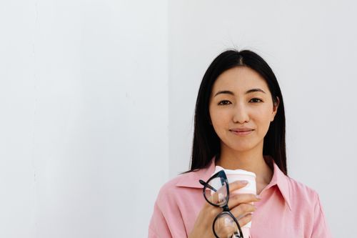 Free Portrait of a smiling woman holding a coffee cup and glasses indoors. Stock Photo