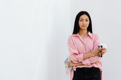 Free Asian woman in a pink shirt holding glasses, standing against a white background. Stock Photo