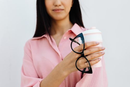 Free Close-up of a woman in a pink blouse holding eyeglasses and a reusable coffee cup, showcasing a minimalist style. Stock Photo